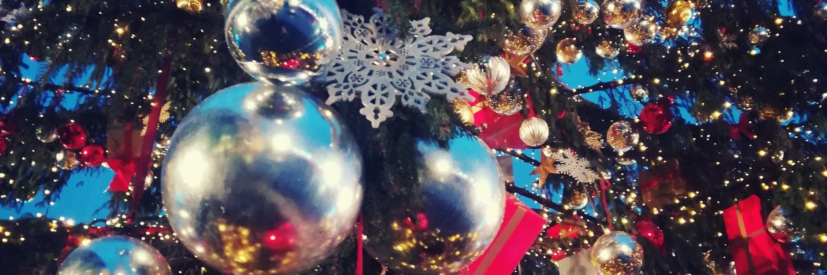 Weihnachtsbaum reichlich geschmückt mit Kugeln Geschenken, Lichterketten und Sternen. Auf dem Bild stehen die Kugeln im Fokus