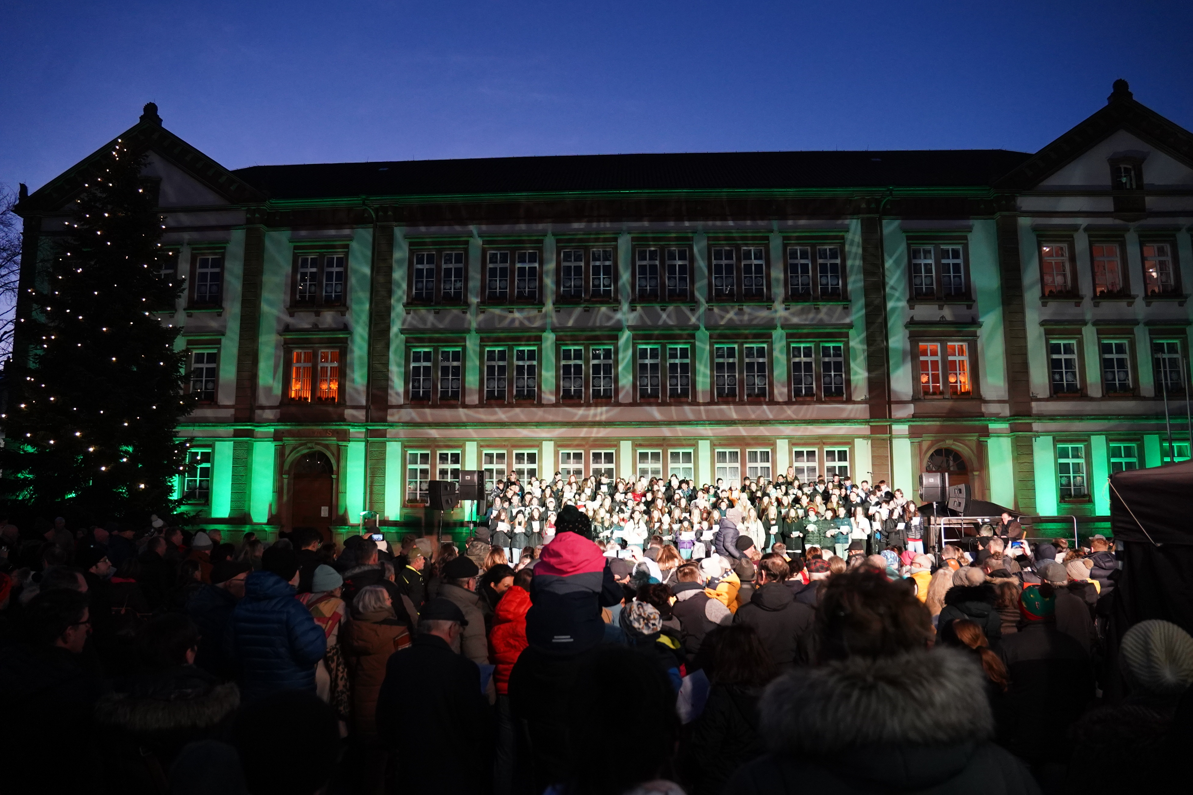 die Sänger stehen auf einer Bühne auf dem Exerzierplatz. Dahinter sieht man das Rathaus. 