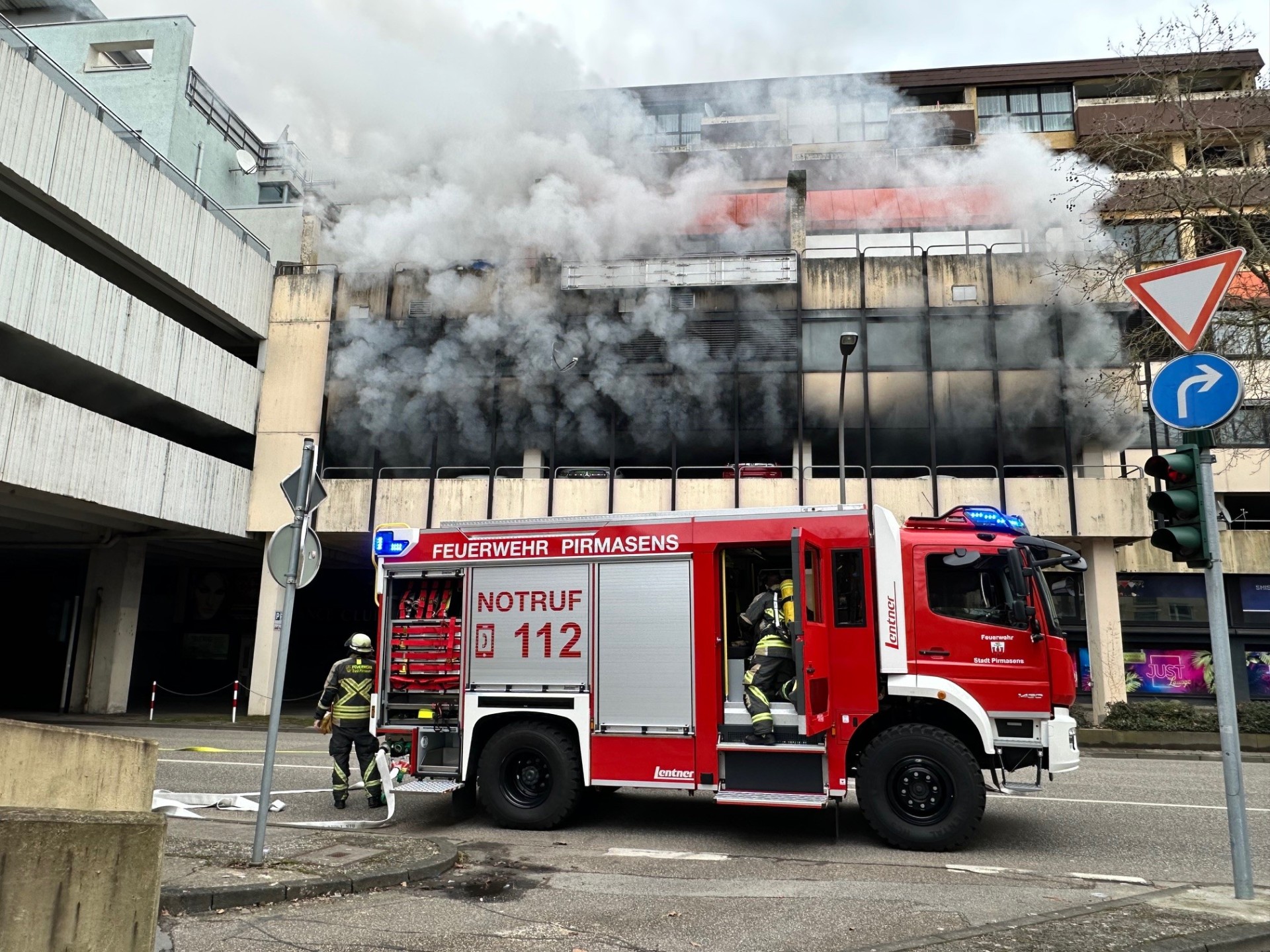 Brand im Parkhaus Schaeferstraße.jpg Ein Feuerwehrauto steht präsent im Bild. Dichter schwarzer Rauch dringt aus dem Parkhaus heraus.