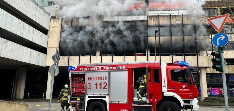 Brand im Parkhaus Schaeferstraße.jpg Ein Feuerwehrauto steht präsent im Bild. Dichter schwarzer Rauch dringt aus dem Parkhaus heraus.