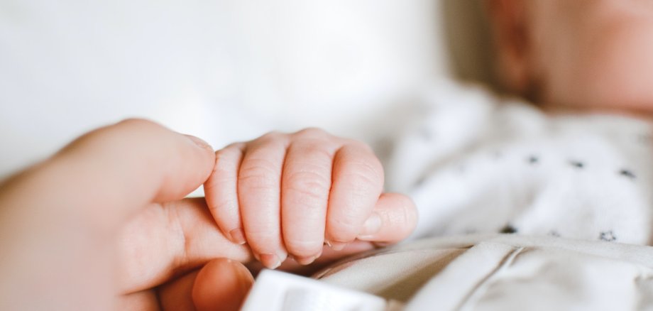 Die Hand eines Neugeborenen umschließt den Finger eines Erwachsenen