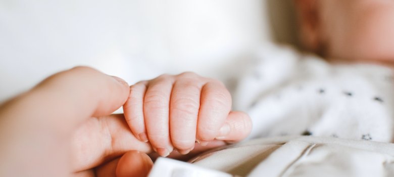 Die Hand eines Neugeborenen umschließt den Finger eines Erwachsenen