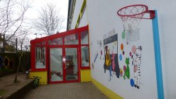 KiTa Ruhbank Abgebildet ist der Eingangsbereich der Kita mit Wandgemälde (verschiedene Tiere mit bunten Bällen) und Basketballkorb