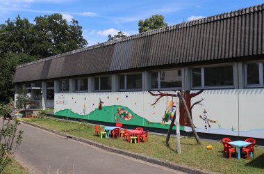 Abgebildet ist das Gebäude der Kita mit Wandgemälde (verschiedene Jahreszeitenmotive vom Samselo) 