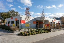 Kita Windsberg auf dem Bild ist die Kita Windsberg zu sehen. Vor dem Gebäude sind Bäume und Busche zu sehen.