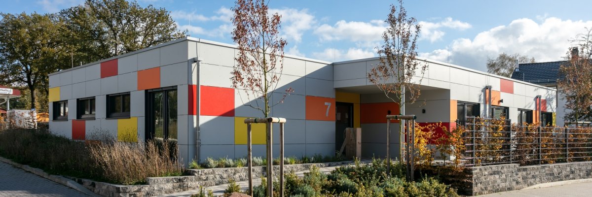 auf dem Bild ist die Kita Windsberg zu sehen. Vor dem Gebäude sind Bäume und Busche zu sehen.