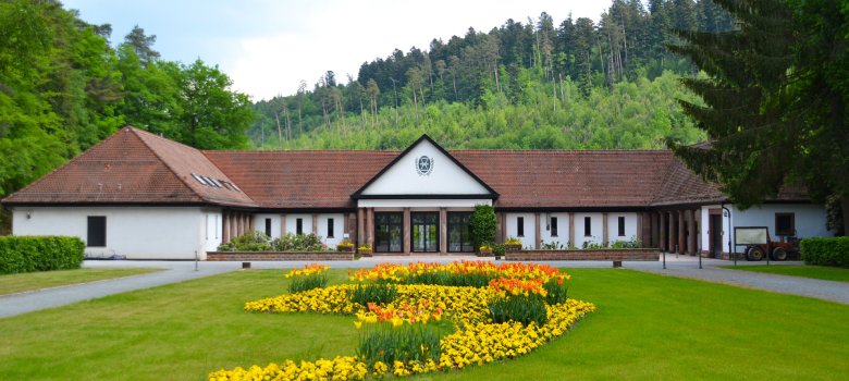 Zu sehen ist die Rückseite der Aussegnungshalle am Waldfriedhof mit dem davor angelegten Blumenbeet mit Frühjahrsflor