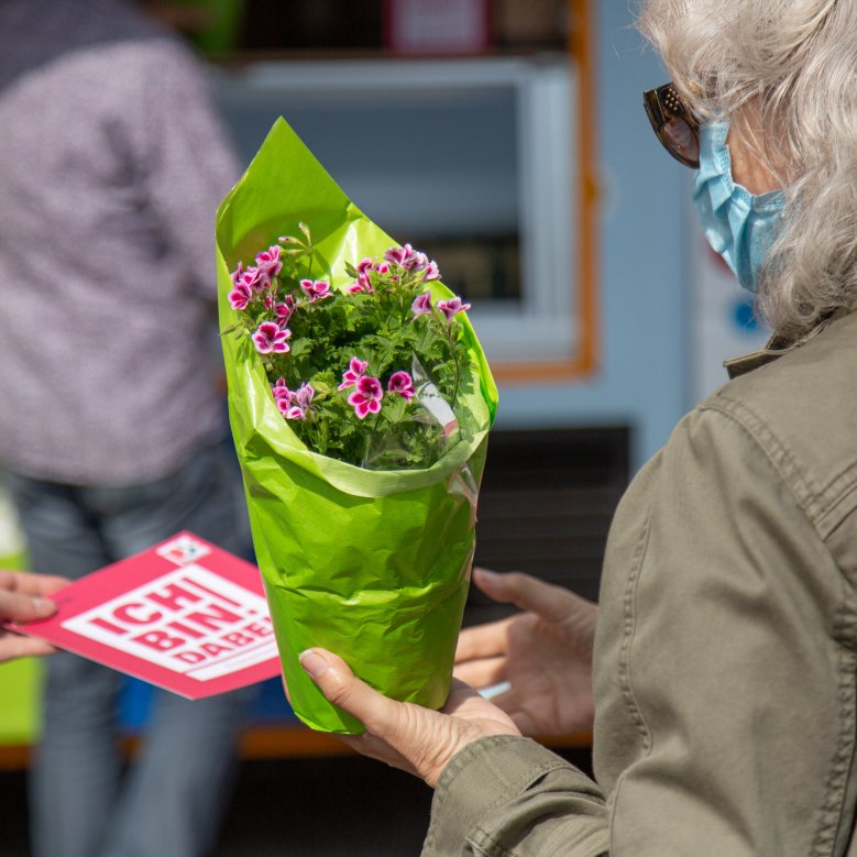 Mit der Ideenkarte wird auch ein kleiner Blumenstock an eine Bürgerin übergeben