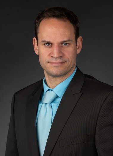 Portraifoto von Denis Clauer vor neutralem Hintergrund im Anzug