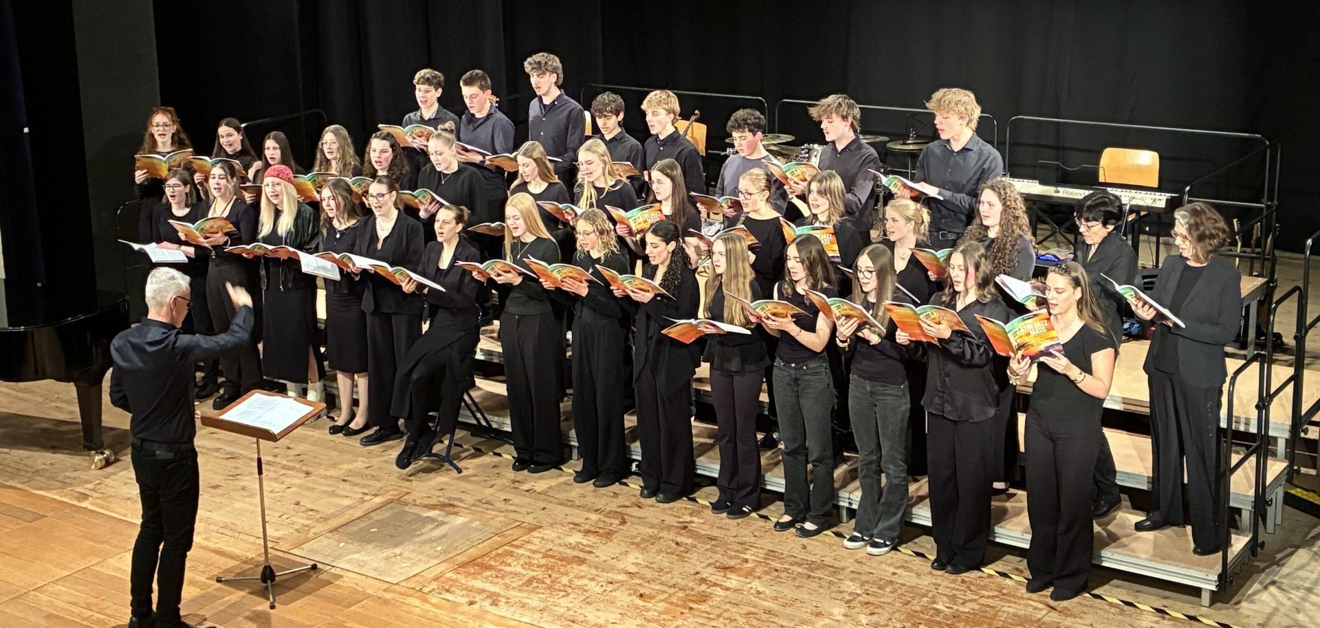Der Kant-Kammerchor unter Leitung von Volker Christ begibt sich in „Latin Jazz Mass“ in die Welt lateinamerikanischer Rhythmen. Jugendchor in schwarzer Kleidung singt auf einer Bühne, während ein Dirigent vor dem Ensemble den Takt vorgibt.