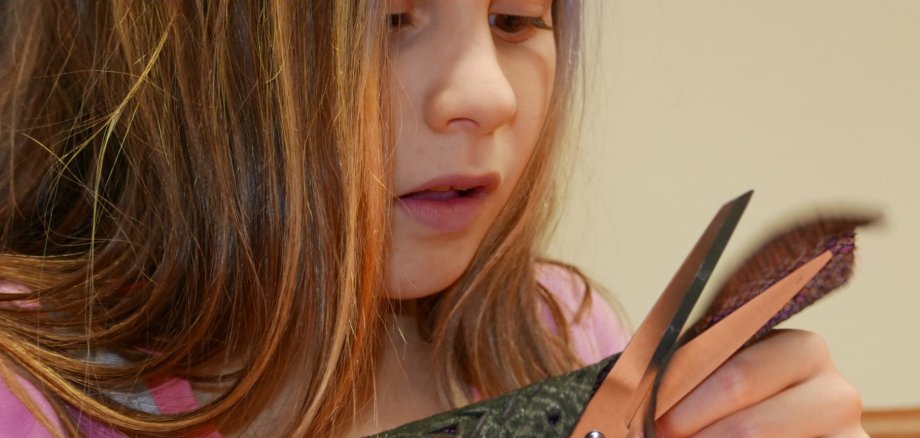 Ein Kind schneidet mit einer Schere vorsichtig Löcher in ein Blatt und konzentriert sich dabei auf die Bastelarbeit.