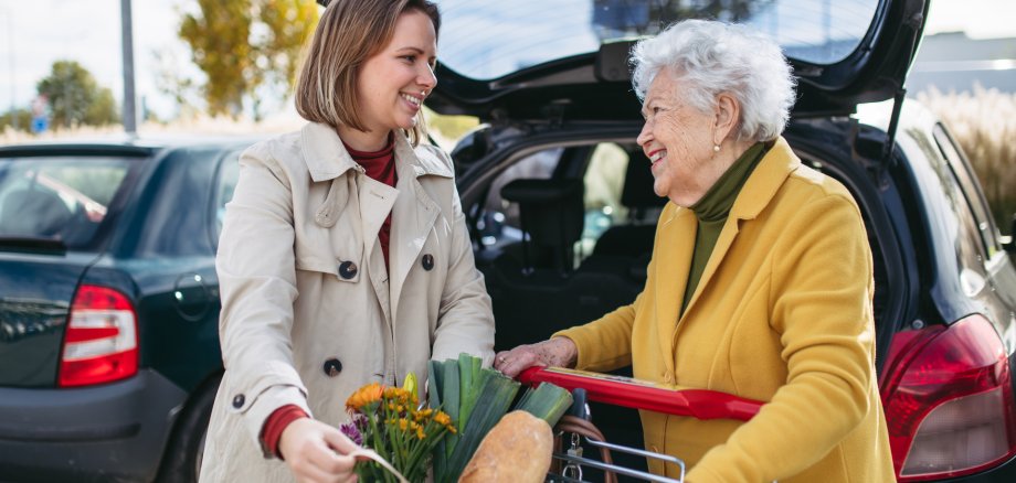 Mature granddaughter helping grandmother load groceries in to the car. Senior woman shopping at the shopping center.