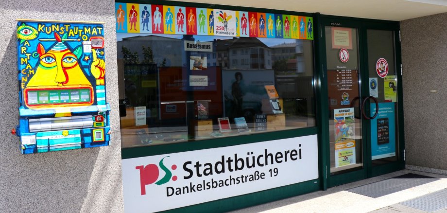 Haupteingang Stadtbücherei Eingang der Stadtbücherei in der Dankelsbachstraße 19 mit großer Fensterfront und Beschilderung „ps: Stadtbücherei“. Links an der Wand ein bunt gestalteter Kunstautomat; im Schaufenster Bücher und Plakate.