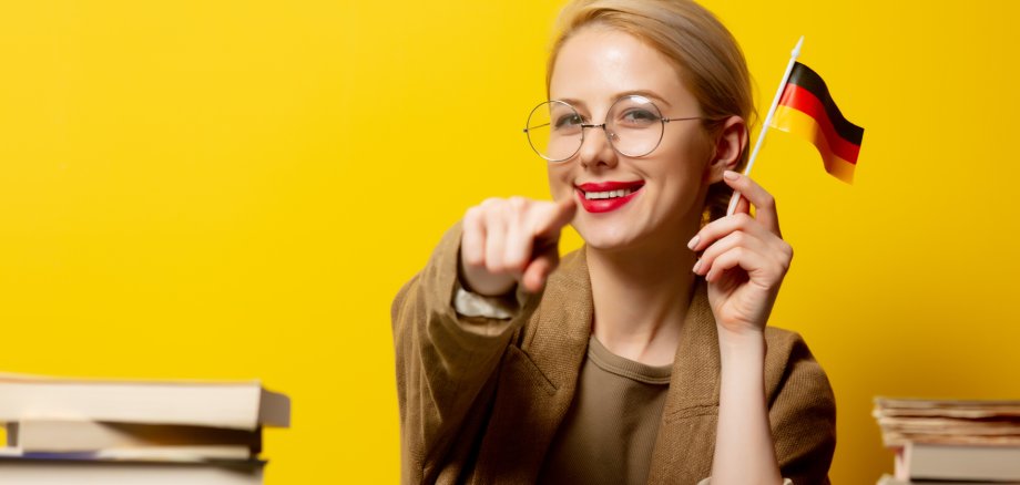 Style blonde woman sitting at table with books and flag of Germa
