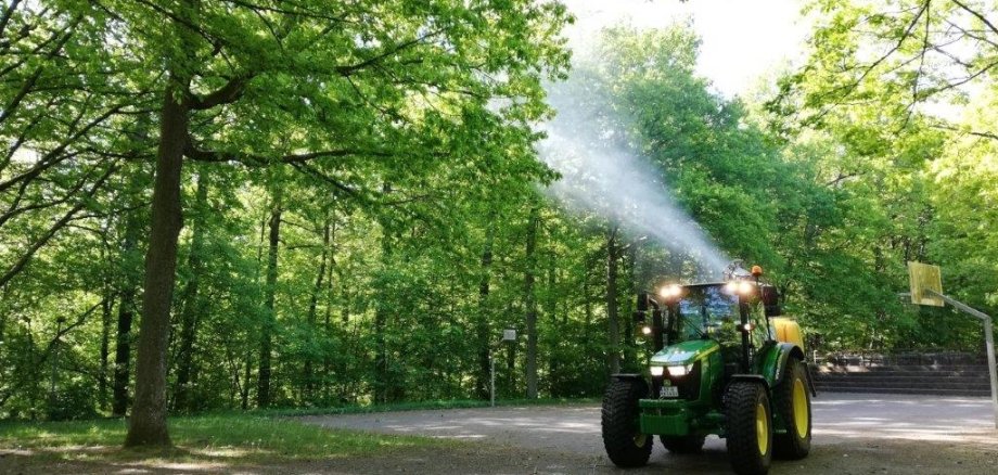 Traktor spritzt mit Wasser auf Bäume zwecks Bekämpfung Eichenprozessionsspinner
