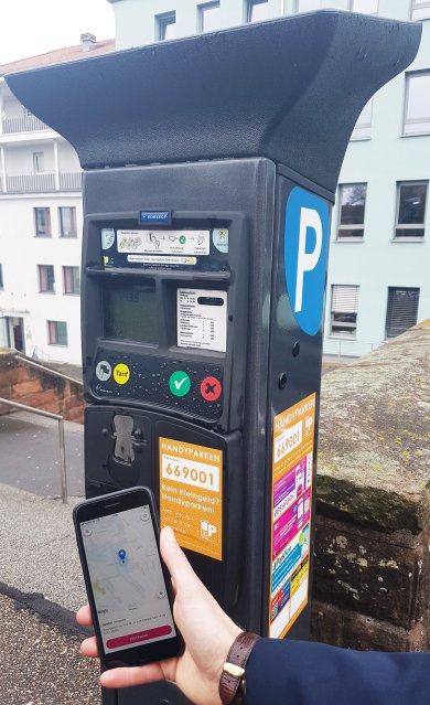 Handyparken mit Parkscheinautomat und Smartphone im Vordergrund 