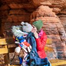 Mama küsst kleines Kind in der Trage vor der Schillerwand