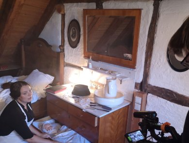 Dreh im Häusel. Gezeigt wird eine Frau in zeitgenössischer Kleidung mit einer Puppe in einer Schublade und ein Kameramann