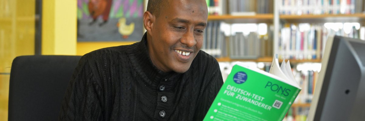 Ein lächelnder Mann mit Migrationshintergrund arbeitet mit einem Sprachkurs in Buchform