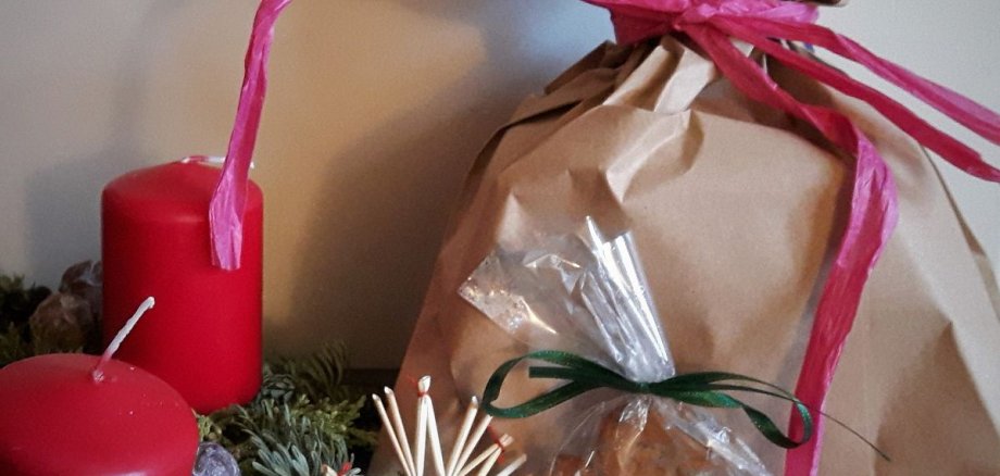 Lebkuchenmännchen, braune Geschenktüte mit pinker Schleife und ein Adventskranz mit 2 roten Kerzen
