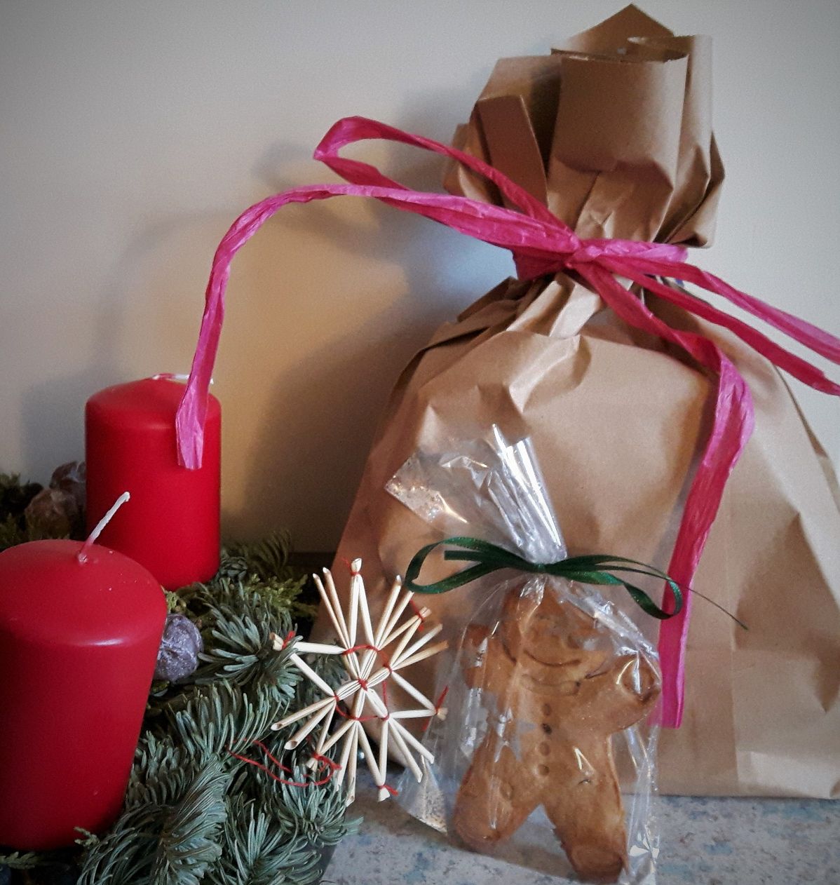 Lebkuchenmännchen, braune Geschenktüte mit pinker Schleife und ein Adventskranz mit 2 roten Kerzen