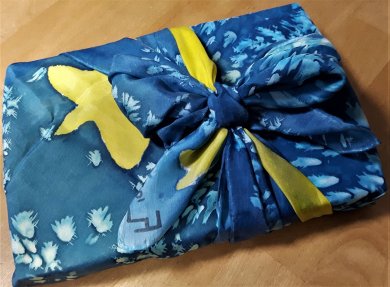 in ein Tuch eingepacktes Geschenk. Tuch hat die Farben blau und gelb in Aquarelloptik