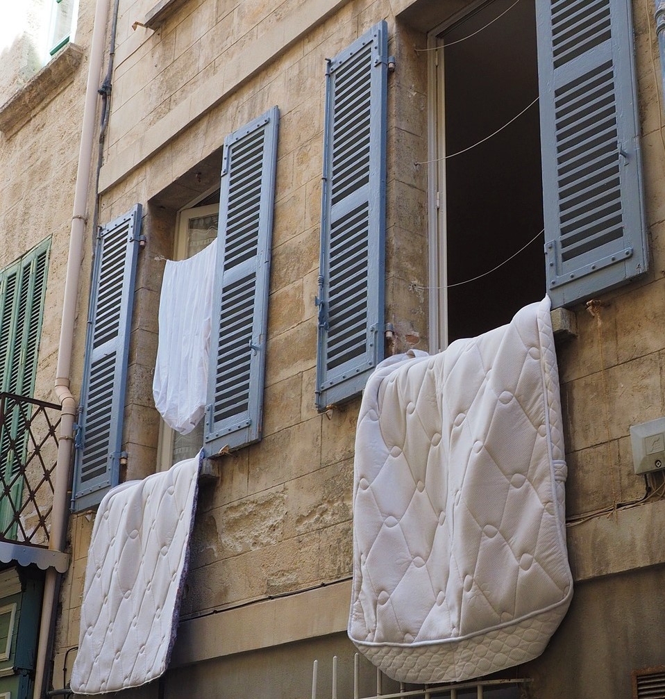 geöffnete Fenster von außen, aus denen Bettdecken und Kleider hängen um zu lüften
