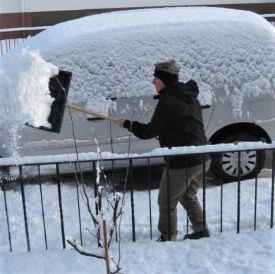 Person beim Schneeräumen mit einen schneebedeckten Auto im Hintergrund