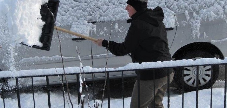Schneeräumen Person beim Schneeräumen mit einen schneebedeckten Auto im Hintergrund